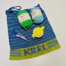 Load image into Gallery viewer, A KREL branded pom pom kit displayed, including a maker, two balls of yarn in green and blue, and a pair of scissors on a striped background.