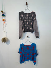 Load image into Gallery viewer, Two sweaters hanging on hooks against a white wall. The top sweater is gray with a geometric pattern including the words 'INTERKNOT', and the bottom sweater is blue with a similar geometric pattern.