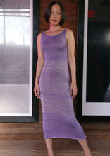 Load image into Gallery viewer, A woman standing in a room with a wooden background, wearing a purple, metallic knit maxi dress with a tank top cut and a flared skirt.