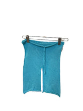 Load image into Gallery viewer, A pair of blue cotton drawstring knit shorts for toddlers, displayed on a hanger amidst various fabric swatches.
