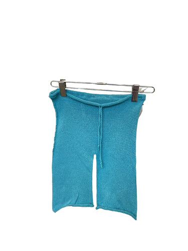 A pair of blue cotton drawstring knit shorts for toddlers, displayed on a hanger amidst various fabric swatches.