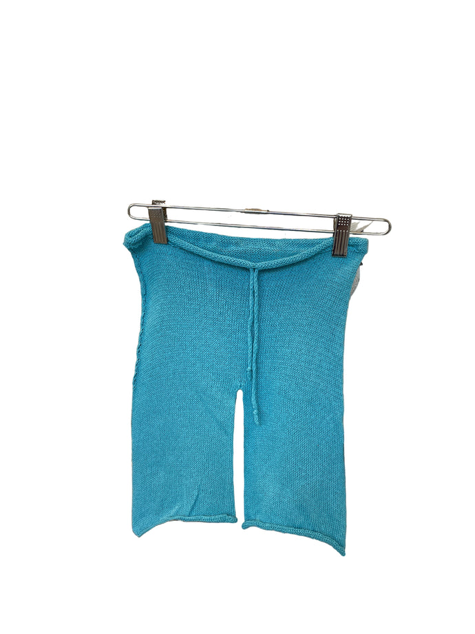A pair of blue cotton drawstring knit shorts for toddlers, displayed on a hanger amidst various fabric swatches.